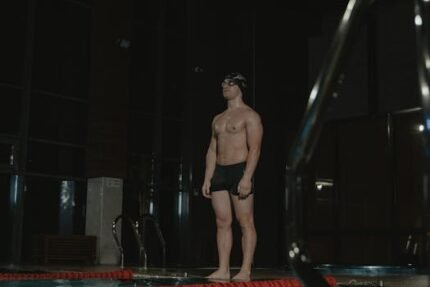 An athletic male swimmer stands ready for action at an indoor pool facility.